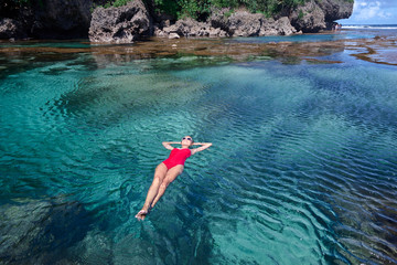 Summer vacation. Young woman in red swimsuit bathing at sea natural pool.
