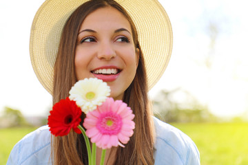 Spring girl holds flowers looking to the side outdoor. Beautiful smiling young woman with hat holding flowers in park and looks around.