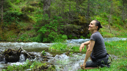 Young hiker woman sitting by a mountain stream, enjoys spending free time at nature