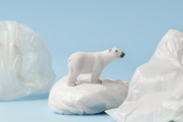 White polar bear on plastic bag on blue background, plastic pollution and climate change concept