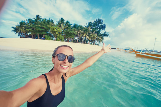 Traveling in Philippines. Happy young woman taking selfie while bathing near small island with white sand tropical beach.