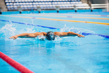 Athletic man swimming in butterfly style in the swimming pool with clear blue water.