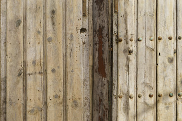 Old wooden door in brown tones with nails and rusty hardware in a ruined house.