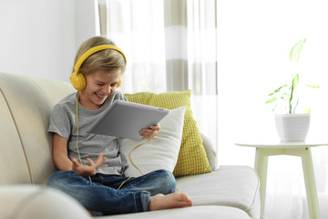 Cute little boy with headphones and tablet listening to audiobook at home