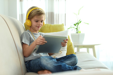 Cute little boy with headphones and tablet listening to audiobook at home