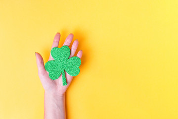 Woman holding shamrock symbol for Saint Patrick's Day on bright yellow background. Minimalistic St.Patrick's Day card, top view, copy space. Holiday background overhead