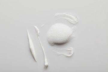 Top view of gel and cosmetic cream brushstrokes with soap foam on grey background