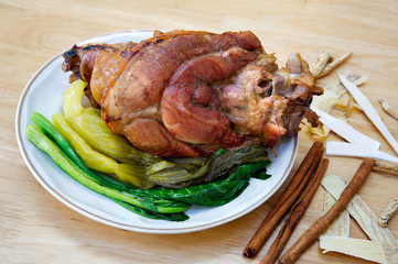 Stewed leg pork without fat with vegetables in white dish and pile of chinese herbs on brown wooden table
