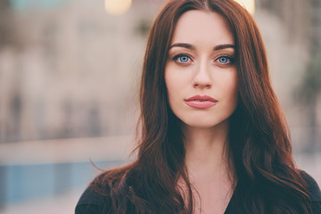 Close-up portrait of beautiful caucasian woman with charming smile and long hair on the city street.