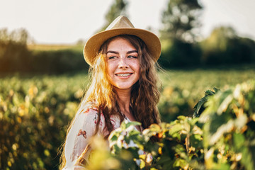 beautiful woman with long curly hair and freckles face on currant field background. Girl in a light dress walks in the summer sunny day