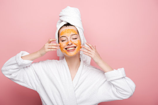 smiling girl with citrus facial mask touching face with closed eyes on pink background