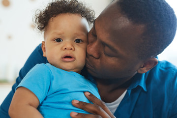 Close up portrait of happy African-American father kissing cute little boy in home interior, copy space
