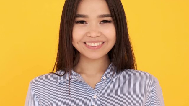 Asian young girl on yellow background draws in air heart. token of love close up