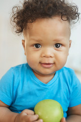 Vertical portrait of cute African-American boy holding green apple and smiling at camera