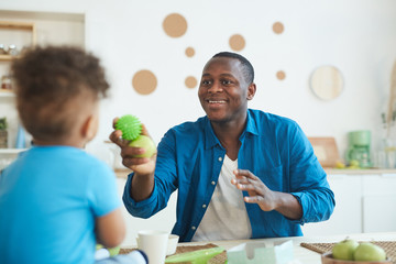 Portrait of happy African-American father playing ball with cute little boy in home interior, copy space