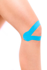 Studio shot of a female patient with kinesio tape on her knee, isolated over white. Kinesiology, physical therapy, rehabilitation background. Cropped shot close up.