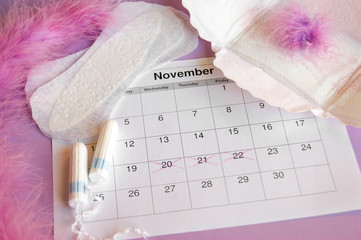 Menstrual pads and tampons on menstruation period calendar with on lilac background.