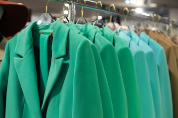 Hangers with spring's women's  wear in shop.  Colorfull green, blue and beige classic coats of spring collection