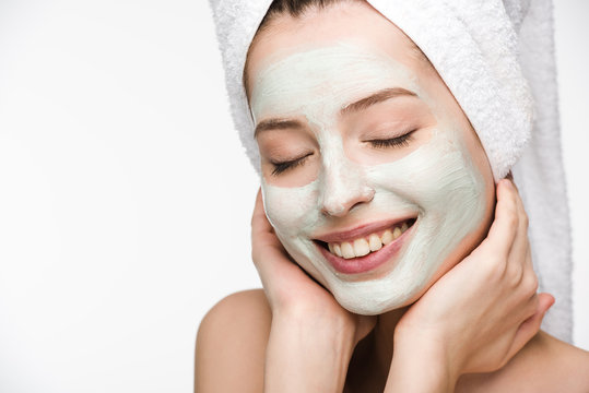 Smiling Girl With Facial Nourishing Mask And Towel On Head Touching Face With Closed Eyes Isolated On White