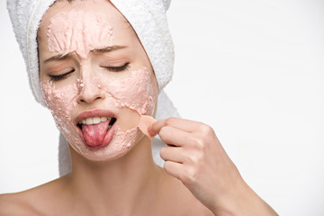 displeased girl removing peeling mask from face and sticking out tongue isolated on white