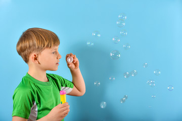 Boy in a green T-shirt blows air bubbles on a blue background.