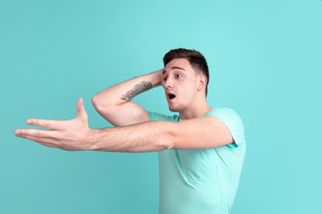 Fototapeta premium Shocked, astonished. Caucasian young man's portrait isolated on blue studio background. Beautiful male model in casual style, pastel colors. Concept of human emotions, facial expression, sales, ad.