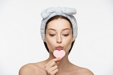 attractive girl kissing heart-shaped cosmetic sponge isolated on white