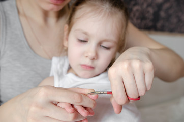 mother cuts her daughter's nails with scissors in the bedroom - focus on her hands. baby hygiene
