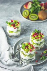 Healthy breakfast: yogurt parfait with granola and kiwi decoration pomegranate and mint on a gray background