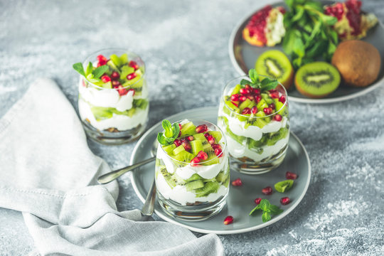 Healthy breakfast: yogurt parfait with granola and kiwi decoration pomegranate and mint on a gray background
