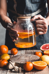 A man pours citrus tea on a wooden table. Healthy drink, vintage style. Vegan, eco products.