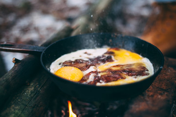 Fried eggs with bacon in a pan in the forest. Food at the camp. Fried egg with bacon on fire. Picnic