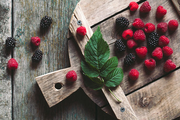blackberries and raspberries on a cutting board. wooden background, vintage style