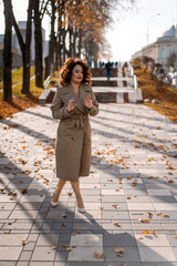 a young woman walks through the autumn city, a happy body female with curly hair in a raincoat.