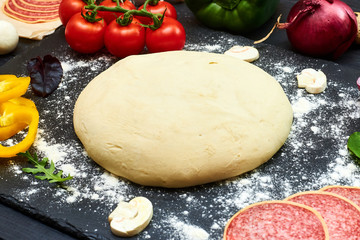 Pizza dough with ingredients on a dark background.