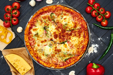 Pizza with mozzarella cheese, tomatoes, mushrooms, pepper on a dark wooden background.