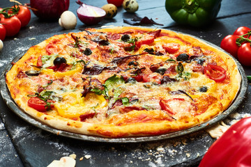 Pizza with mozzarella cheese, tomatoes, mushrooms, peppers, herbs on a dark wooden background.