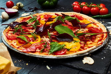 Raw pizza with mozzarella cheese, meat, tomatoes, mushrooms, peppers, herbs on a dark wooden...