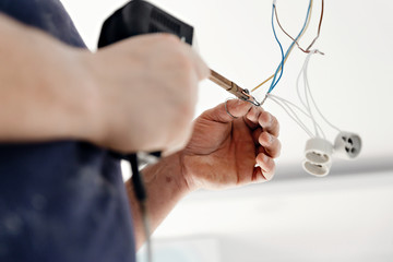 a male electrician is standing on the stairs holding wiring in his hands and stripping,repairing...