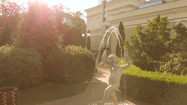 Splashing fountain sculpture of boy with fishes in his hands. Mansion yard garden. Warm sunny day.
