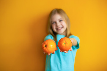 Cute baby 8 years old on an orange background, blonde pretty girl with appelsins in her hands smiles
