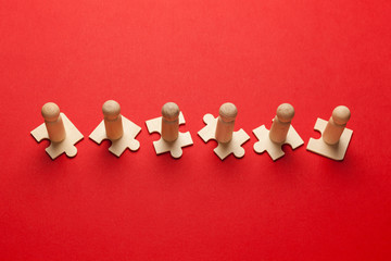 Obraz premium Wooden figures on puzzles on red background as a symbol of team building. Organization group people in business. Cooperation and partnership.