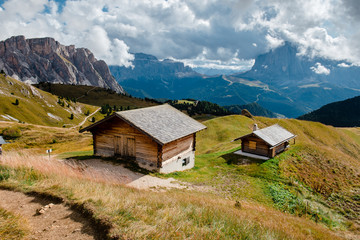Fototapeta na wymiar Landscape with small wooden houses on the background of the Alpine mountains. Hike to the tops of Seceda. Sunny landscape in South Tyrol