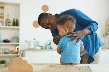 Portrait of adult African-American man caring for cute toddler alone at home, copy space
