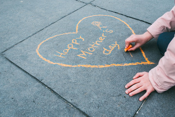 a girl painting the heart of Mother's Day with orange chalk on the floor seen up close