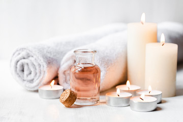 Obraz na płótnie Canvas Concept of spa treatment in salon. Natural organic oil, towel, candles as decor. Atmosphere of relax, serenity and pleasure. Anti-stress and detox procedure. Luxury lifestyle. White wooden background