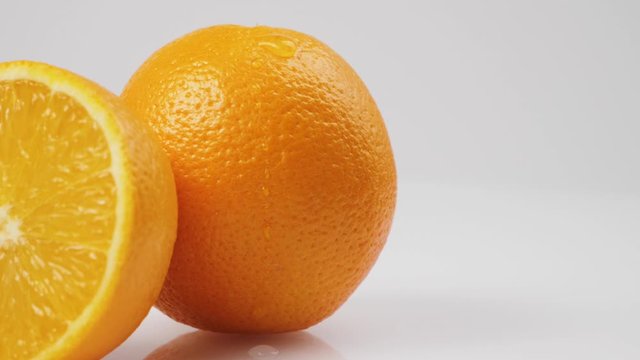 Middle Shot Of Drop Of Water Slowly Flows Down A Fresh Orange On A White Table Against White Background, In Isolation