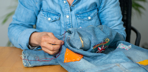 elderly woman hands sewing on fabric jeans