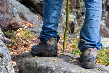 Legs of a tourist in hiking boots on a walk in the autumn along a mountain trail. A man in black boots and blue jeans against a background of mountain boulders. Vacation and adventure concept.