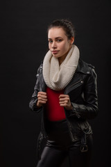 A stylish young woman in a black coat and knitted hat poses on black background. Autumn and winter women's fashion.
